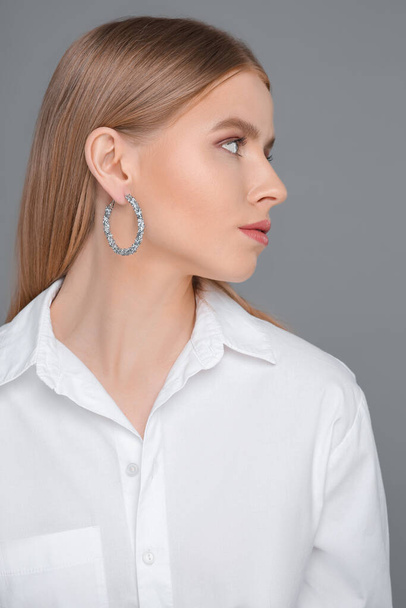 Beautiful young woman with elegant earrings on gray background - Фото, зображення