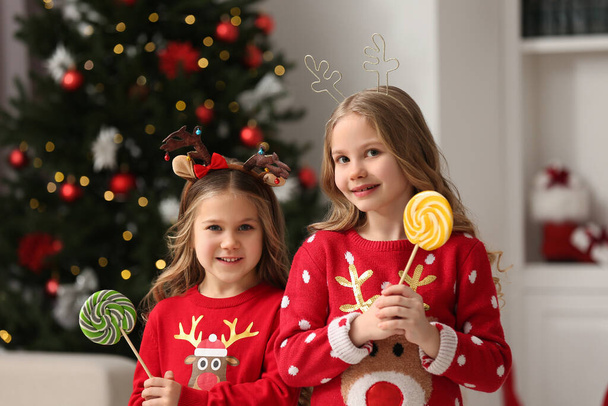 Cute little girls with lollipops near Christmas tree at home - Foto, Imagen