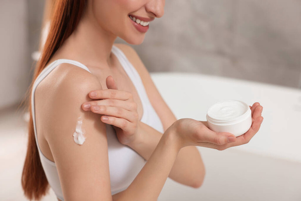 Young woman applying body cream onto shoulder in bathroom, closeup - Photo, image