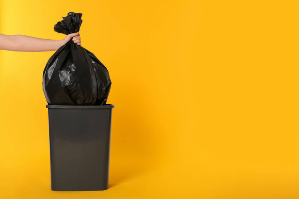Woman holding trash bag full of garbage over bucket on orange background, closeup. Space for text - Foto, Imagem