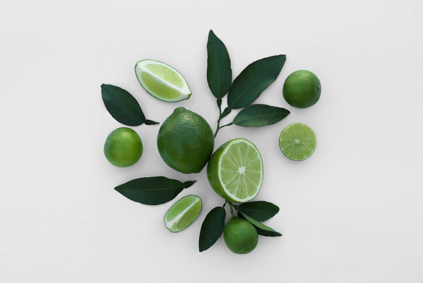 Whole and cut fresh limes with leaves on white background, flat lay - Valokuva, kuva
