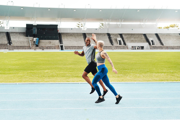 Buen trabajo. Tiro de longitud completa de dos jóvenes atletas que se dan un máximo de cinco durante una carrera en un campo de atletismo - Foto, Imagen