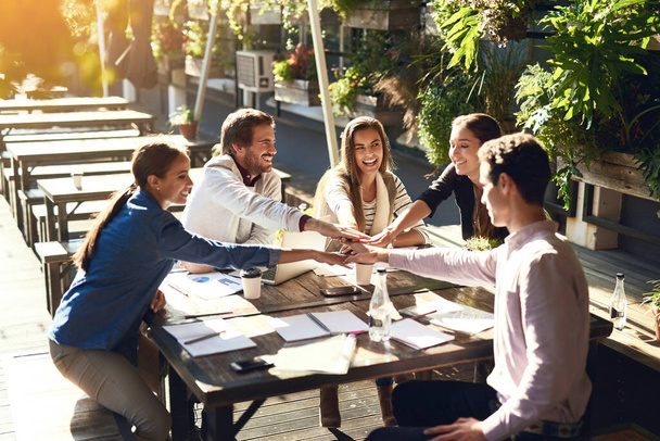 Its just better when you work together. a group of colleagues joining hands in agreement during a meeting at an outdoor cafe - Фото, изображение