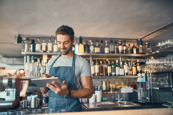 Tecnologia moderna para uma pequena empresa moderna. um jovem usando um tablet digital enquanto trabalhava atrás de um balcão de bar - Foto, Imagem