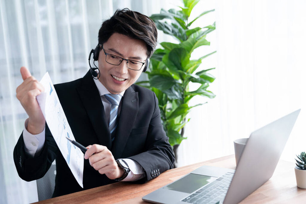 ヘッドフォンを装着したモダンなオフィスでアジアのテレセールスビジネスマンの仕事を自信を持って、オンライン会議でクライアントと顧客にBIダッシュボード分析を提示します。近代的なテレセールスビジネスを成功させます。ジュビラント - 写真・画像