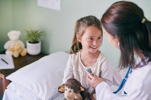 Healthcare, kids and a girl at a woman pediatrician for an appointment or checkup in the hospital. Medical, stethoscope and cardiology with an adorable female child sitting on a bed in the clinic. - Photo, Image