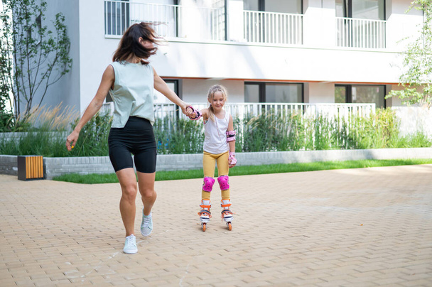 Mother helps daughter learn to roller skate - Fotoğraf, Görsel