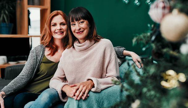 Siamo amici da cosi 'tanto tempo. Ritratto di due attraenti donne di mezza età sedute insieme su un divano accanto a un albero di Natale a casa - Foto, immagini