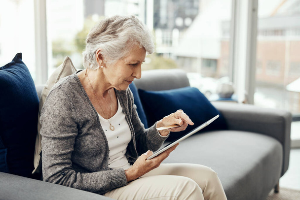 Az online vásárlás energiát takarít meg. egy idős nő, aki digitális táblagépen böngészve tartja a hitelkártyáját. - Fotó, kép