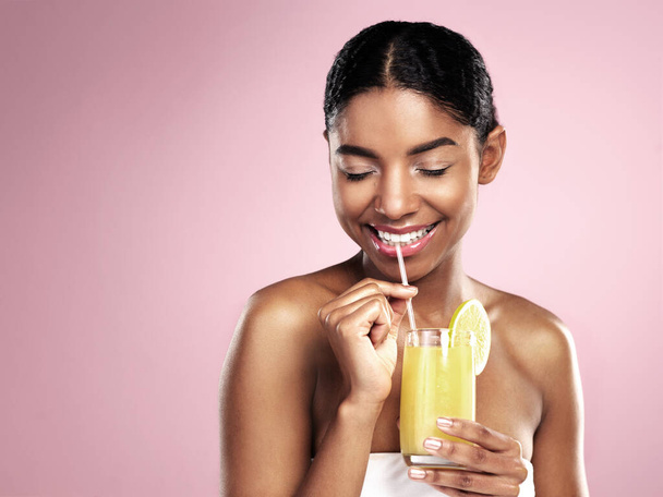 Ευτυχισμένη γυναίκα πίνει χυμό πορτοκάλι στο στούντιο, ροζ φόντο και mockup για υγιή περιποίηση του δέρματος. Αφρικανικό μοντέλο, κοκτέιλ φρούτων και smoothie για διατροφικά οφέλη, φυσική ομορφιά ή βιταμίνη C διατροφή. - Φωτογραφία, εικόνα