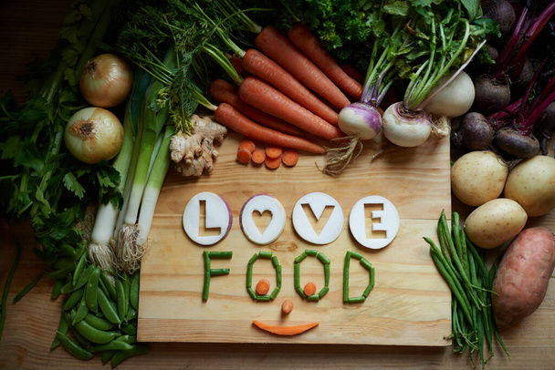 Topraktan yeni çıkmış. Aşkın ve yemeğin yazılı olduğu doğranmış tahtanın üzerinde çeşitli sebzelerden oluşan bir fotoğraf. - Fotoğraf, Görsel