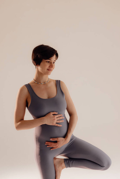Young pregnant woman doing yoga exercises and meditating at studio. Health care, mindfulness, relaxation and wellness concept. - Fotó, kép