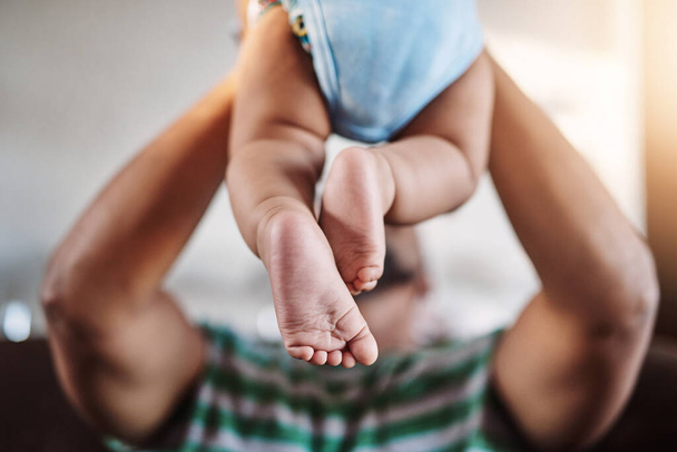 Closeup, legs and baby with father, love and playing with joy, happiness and bonding in the lounge. Zoom, dad and infant in the air, home and games with child development, fun and family on a couch. - Photo, Image