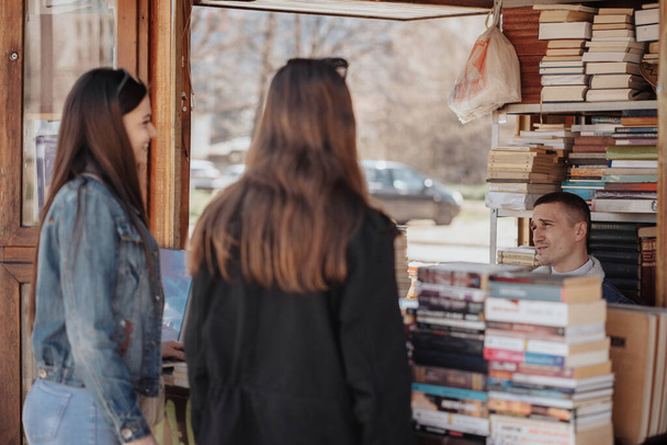 Zwei brünette Mädchen im Gespräch mit dem Buchhändler, während sie in der alten Buchhandlung stehen - Foto, Bild
