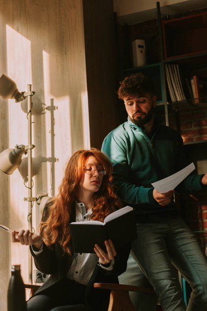 Gorgeous businesswoman with long red hair, reading document about the project to her male colleague. He is disappointed and confused - Фото, зображення