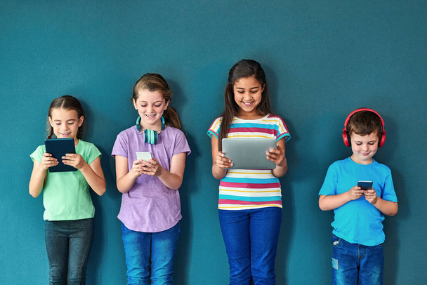 More mobile than ever. Studio shot of a group of kids using wireless technology against a blue background - Φωτογραφία, εικόνα