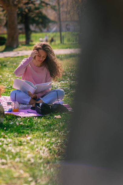 Милая кудрявая девочка учится в парке перед экзаменом на следующей неделе. - Фото, изображение