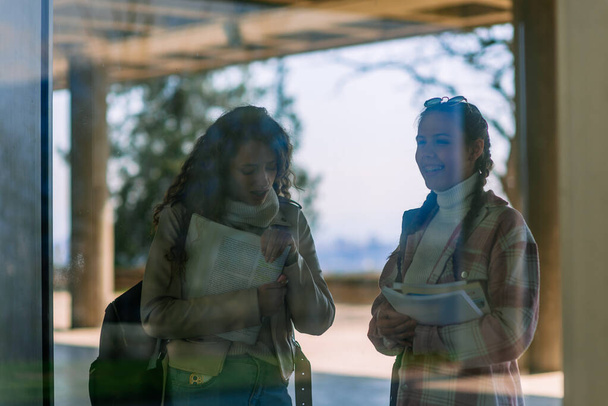 Egy fénykép két kedves középiskolás lányról, akik könyveket tartanak, és viccesen beszélgetnek és mosolyognak. - Fotó, kép