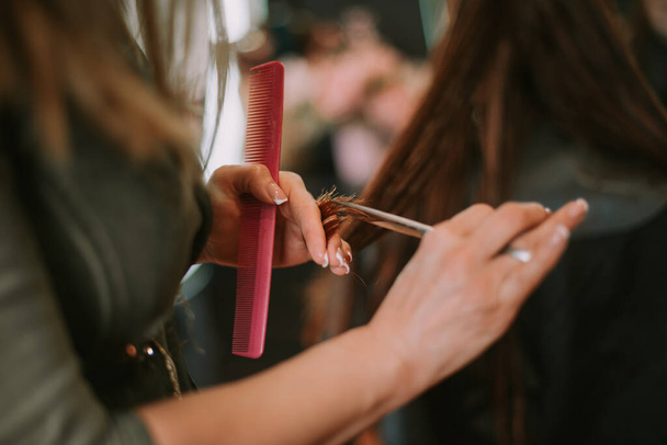 Λεπτομέρειες για κομμωτήριο κοπής βρεγμένα μαλλιά με ψαλίδι κοπής και κρατώντας ροζ χτένα - Φωτογραφία, εικόνα