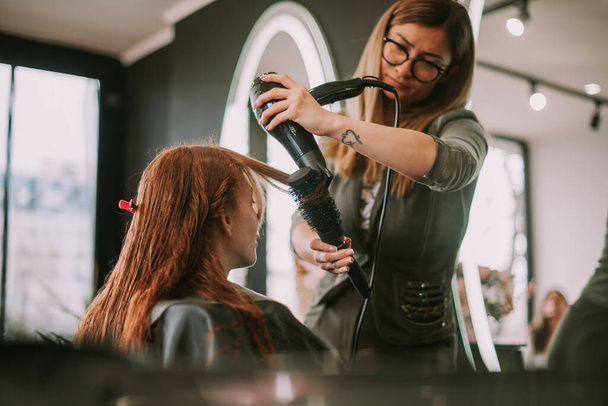 Piękna blondynka fryzjer dmuchanie jej klienci grzywka w salon fryzjerski - Zdjęcie, obraz