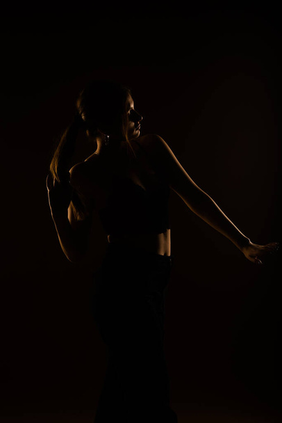 Μια φωτογραφία του σέξι κοριτσιού που ποζάρει με μαύρα ρούχα, σουτιέν και παντελόνια. Αγγίζει τα μαλλιά της με το δεξί χέρι. - Φωτογραφία, εικόνα