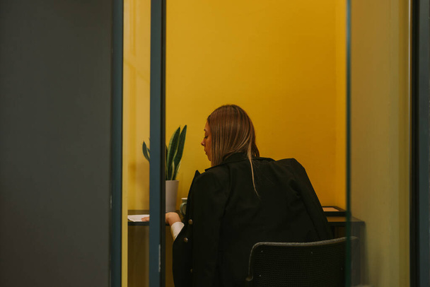 Nahaufnahme einer blonden Geschäftsfrau, die arbeitet und sich die Dokumente ansieht, während sie im kleinen gelben Raum des Co-Working Space sitzt - Foto, Bild