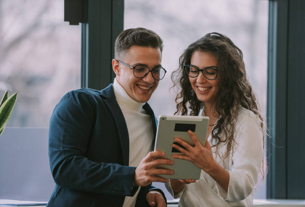 Dwóch współpracowników biznesowych uśmiechających się i patrzących na tablet stojąc w miejscu pracy - Zdjęcie, obraz