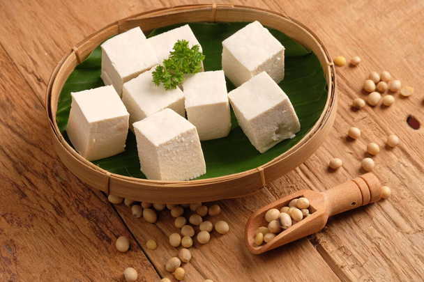 Tofu oder Bohnenquark sind traditionelle Lebensmittel, die aus Sojabohnen hergestellt werden. Tofu in Scheiben geschnitten auf Bambusgeflechtgefäß mit Bananenblatt. tahu putih. Holztisch. Kochlöffel. - Foto, Bild