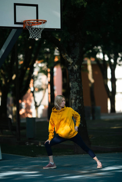 Uma mulher se exercita em um campo de basquete ao ar livre antes de um jogo.  - Foto, Imagem