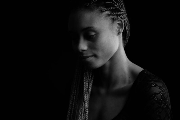 Beautiful young woman with braids studio intimate close up portrait isolated against black background. Black and white image. - Foto, imagen