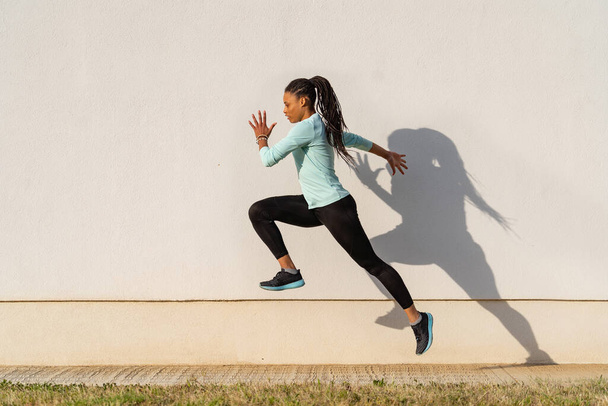 Giovane donna sportiva ritratto correre all'aperto e saltare sullo sfondo della parete. - Foto, immagini