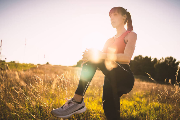 Young sporty woman portrait outdoors in the field at sunset. Back light with flare. Conceptual image of freedom.  - 写真・画像