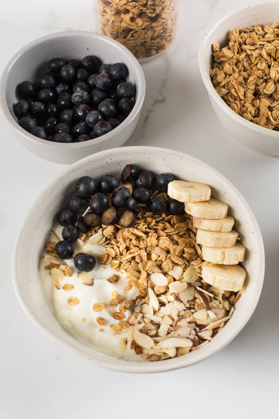 Homemade granola with Greek yogurt, almonds, blueberries and banana in a bowl. Healthy breakfast concept, recipe. - Fotó, kép