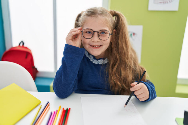 Adorable blonde girl student smiling confident drawing on paper at classroom - Photo, Image