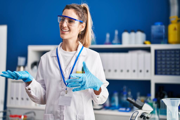 Nuori nainen tiedemies hymyilee luottavainen puhuu laboratoriossa - Valokuva, kuva
