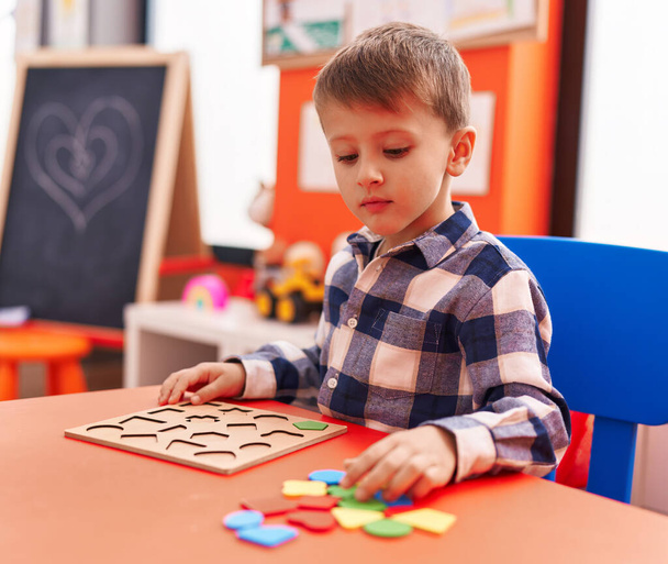 Roztomilý kavkazský chlapec hraje s matematikou puzzle hry sedí na stole ve školce - Fotografie, Obrázek