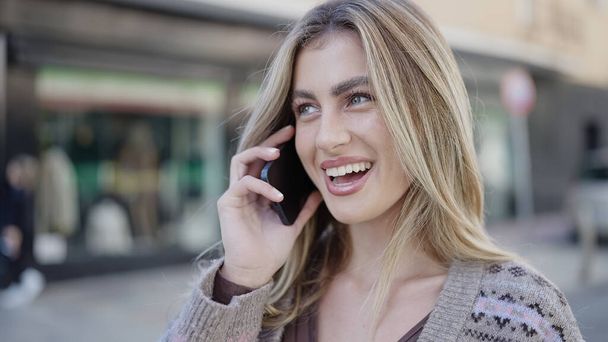 Mladá blondýna žena usmívá sebevědomě mluvit na smartphone na ulici - Fotografie, Obrázek