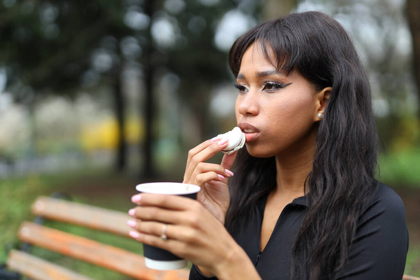 Portrait of an African woman who eats macaroons with coffee in the park. - Photo, Image