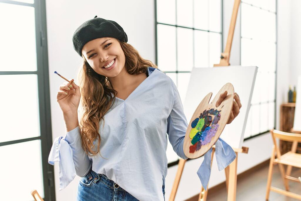 Güzel İspanyol kadın sanatçı gülümsüyor. Resim stüdyosunda fırça ve palet tutuyor. - Fotoğraf, Görsel