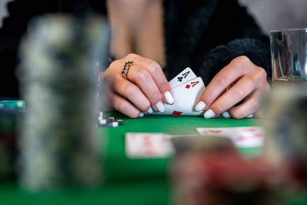 όμορφη νεαρή κοπέλα κάθεται σε ένα τραπέζι πόκερ με χαρτιά στα χέρια της. παιχνίδι πόκερ τύχης. τα χέρια μιας γυναίκας κρατούν χαρτιά πόκερ - Φωτογραφία, εικόνα