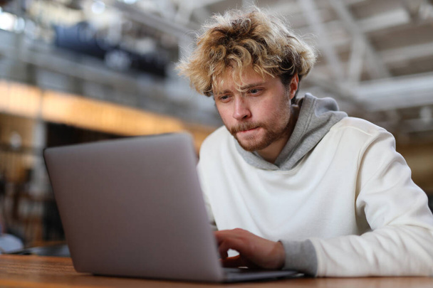 Difficulties in working with a laptop, a concentrated young blond man at the workplace. - Photo, image