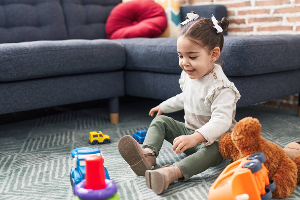 Adorable hispanic girl playing with car toy sitting on floor at home - Foto, Imagem