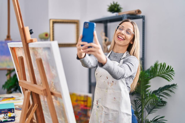 Fiatal nő művész mosolygós magabiztos, hogy szelfi az okostelefon a művészeti stúdióban - Fotó, kép