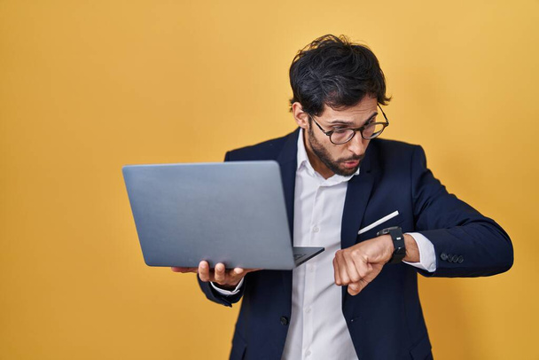 Красивий латинський чоловік працює за допомогою комп'ютерного ноутбука, дивлячись на тривогу годинника, боячись запізнитися
  - Фото, зображення
