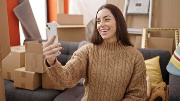 Młoda piękna Latynoska kobieta zrobić selfie przez smartfona siedzi na kanapie w nowym domu - Zdjęcie, obraz