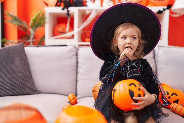 Menina loira adorável vestindo traje de bruxa comendo doce em casa - Foto, Imagem