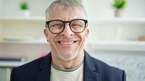 Middle age grey-haired man teacher smiling confident standing at university classroom - Foto, Bild