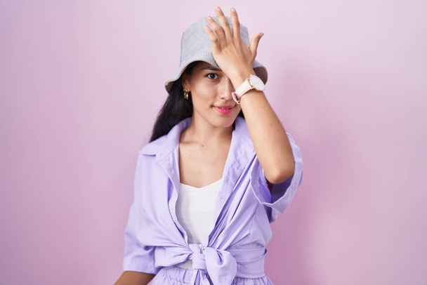 Young hispanic woman standing over pink background wearing hat surprised with hand on head for mistake, remember error. forgot, bad memory concept.  - Foto, imagen