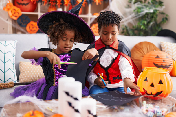 Adorable african american boy and girl having halloween party cutting paper at home - Foto, afbeelding
