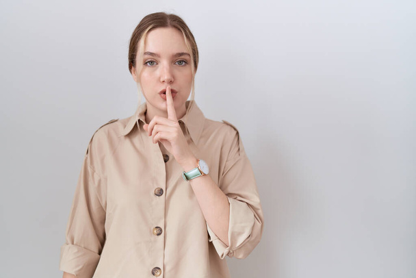 Junge kaukasische Frau in lässigem Hemd, die mit dem Finger auf den Lippen um Ruhe bittet. Schweigen und geheimes Konzept.  - Foto, Bild